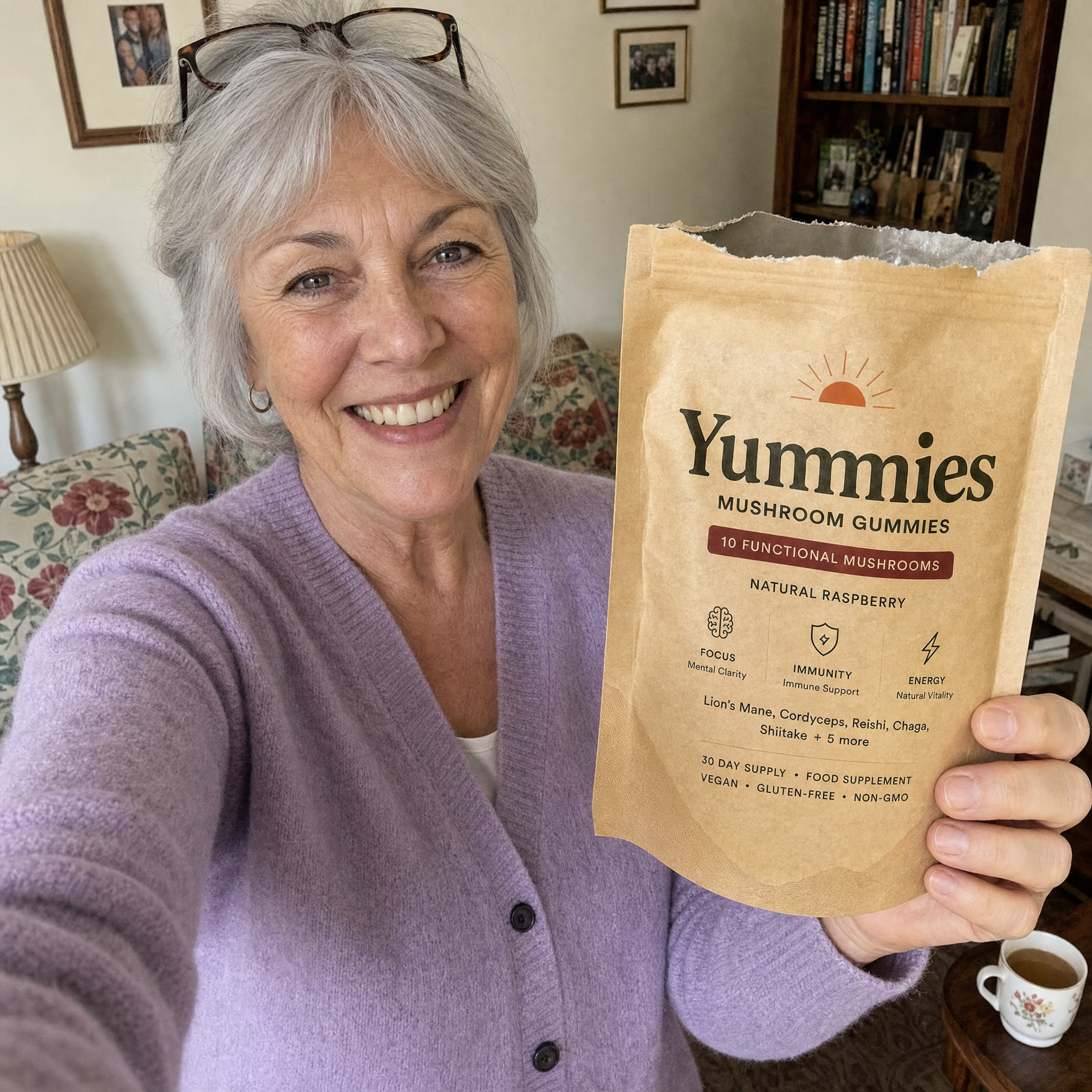 A smiling woman with grey hair holds up a torn-open pouch of Yummies Mushroom Gummies.