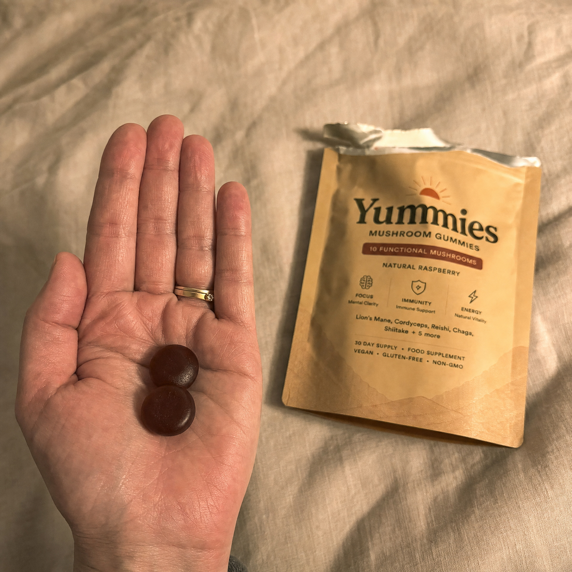 A person holds two Yummies mushroom gummies in their hand next to the product pouch.