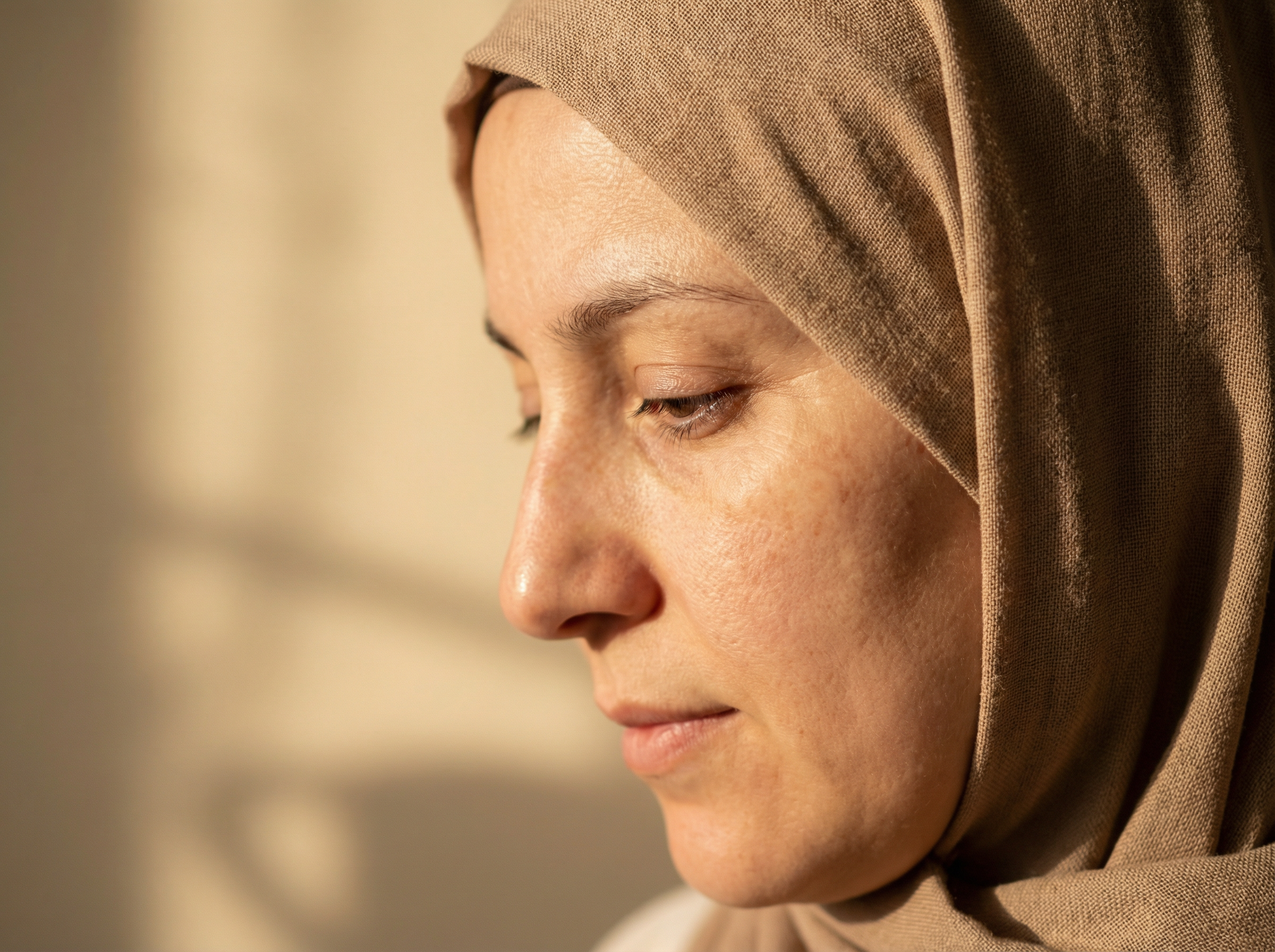 Close-up of a woman wearing a beige headscarf, looking down.