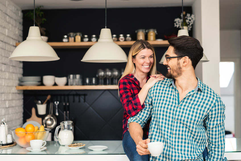 Two people smiling in a modern kitchen with shelves and hanging lights.
