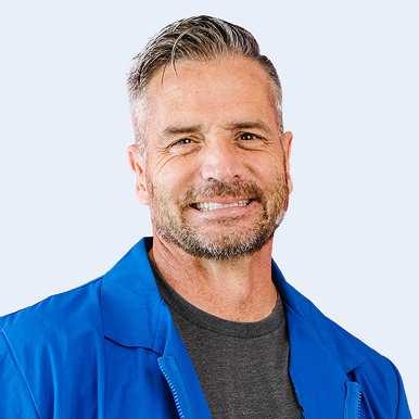 A smiling man wearing a blue jacket over a grey shirt.