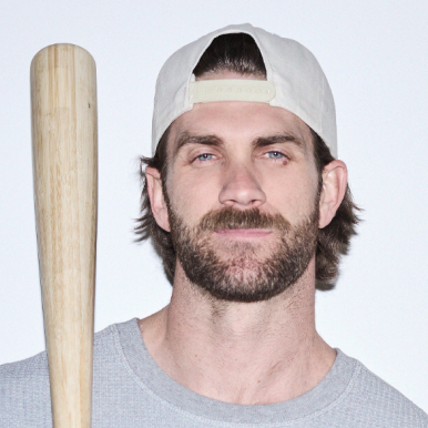 A man wearing a cap holds a baseball bat, looking at the camera.