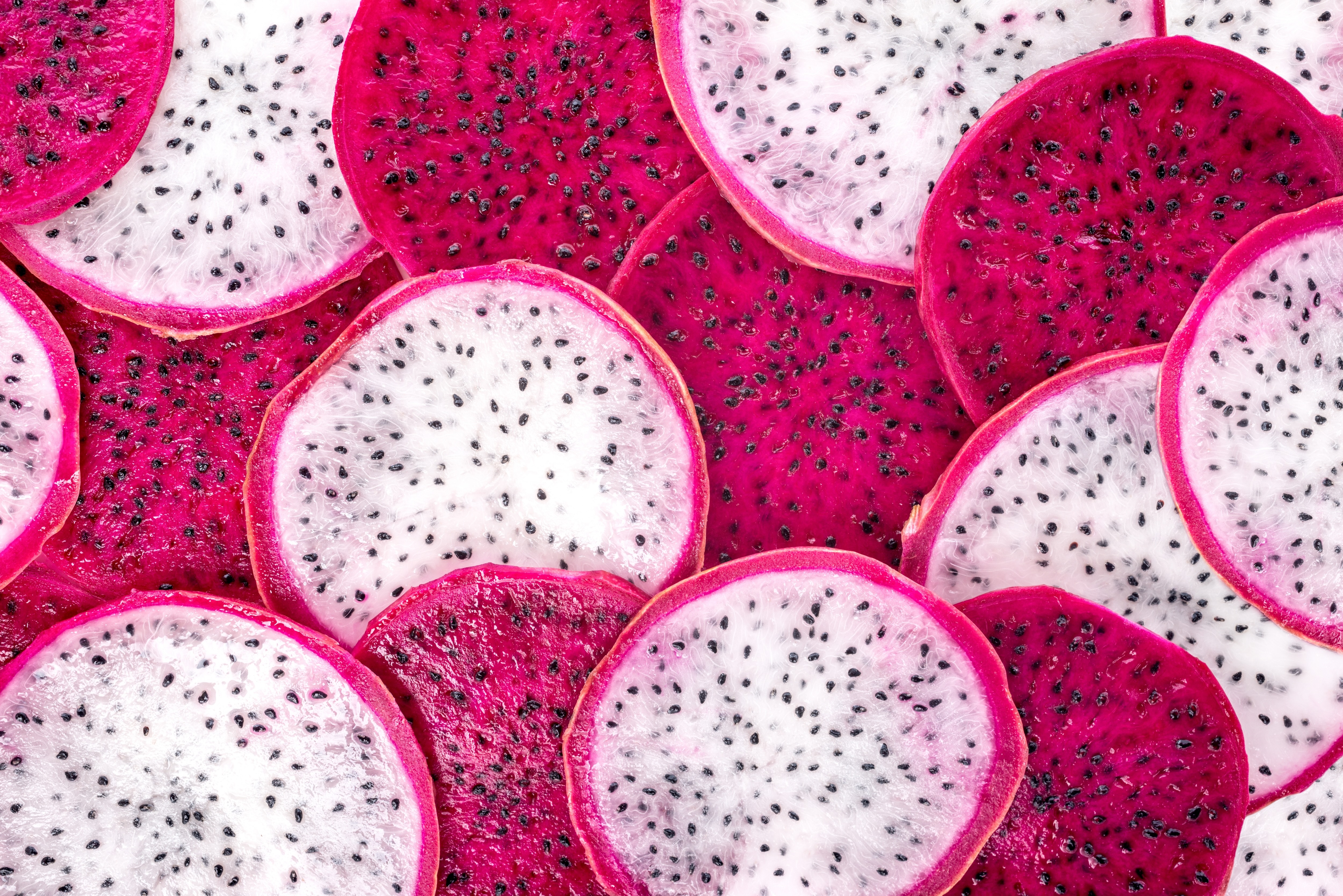 Slices of dragon fruit with white and pink flesh and black seeds.