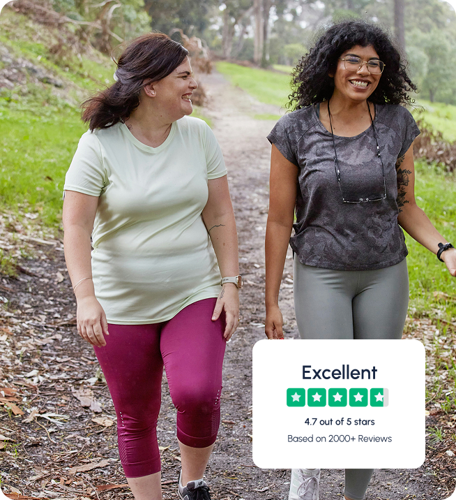 Two women walking on a forest path, smiling and talking.