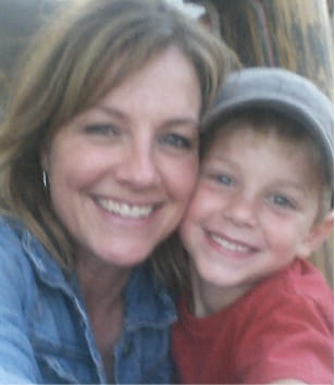 A woman with blonde hair and a young boy in a grey cap smiling for a close-up photo.