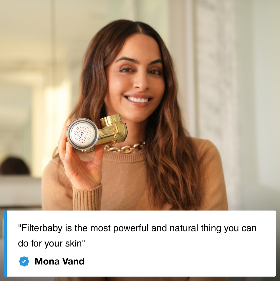 A person smiling and holding a gold shower filter in a well-lit room.