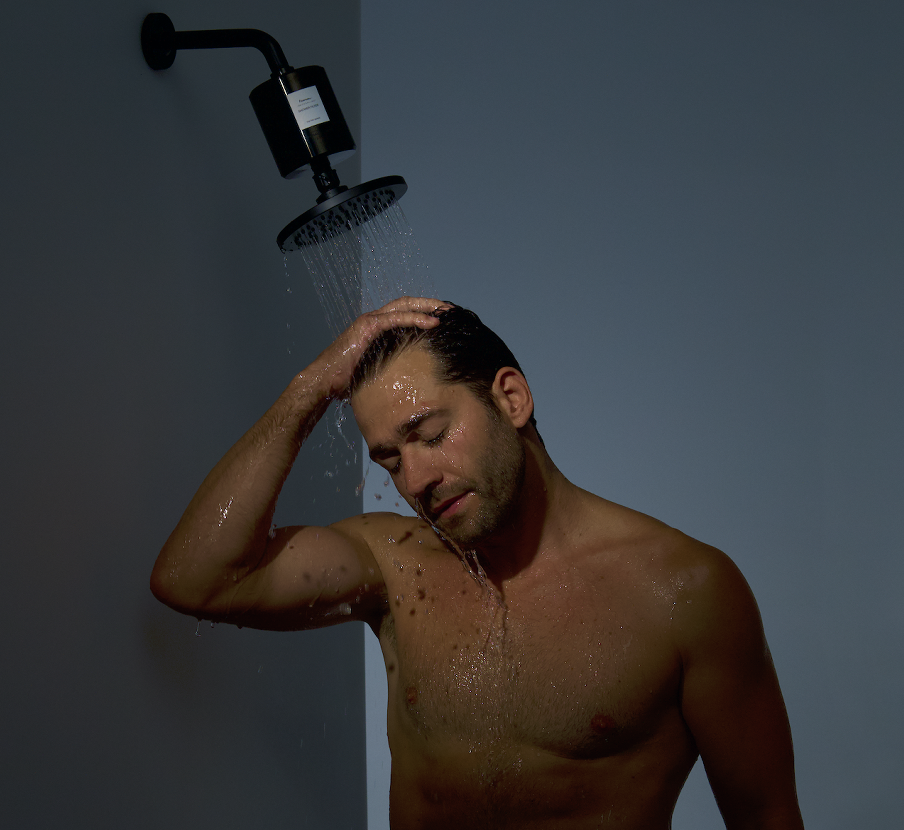 Man showering, water flowing from showerhead, hand on head.