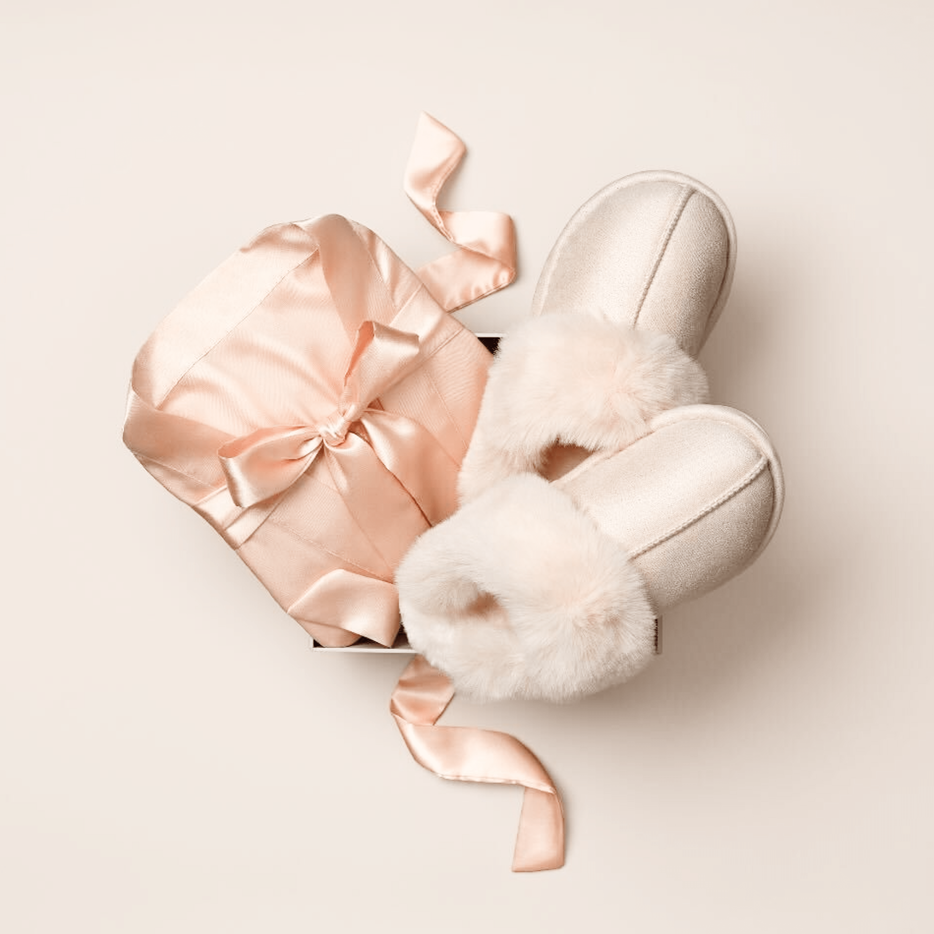 Gift box with pink ribbon and pair of fuzzy slippers on a beige background.