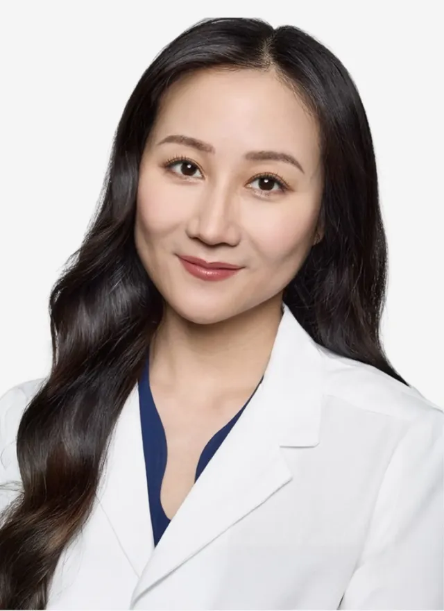 A headshot of an East Asian woman with long dark hair, wearing a white coat and smiling.