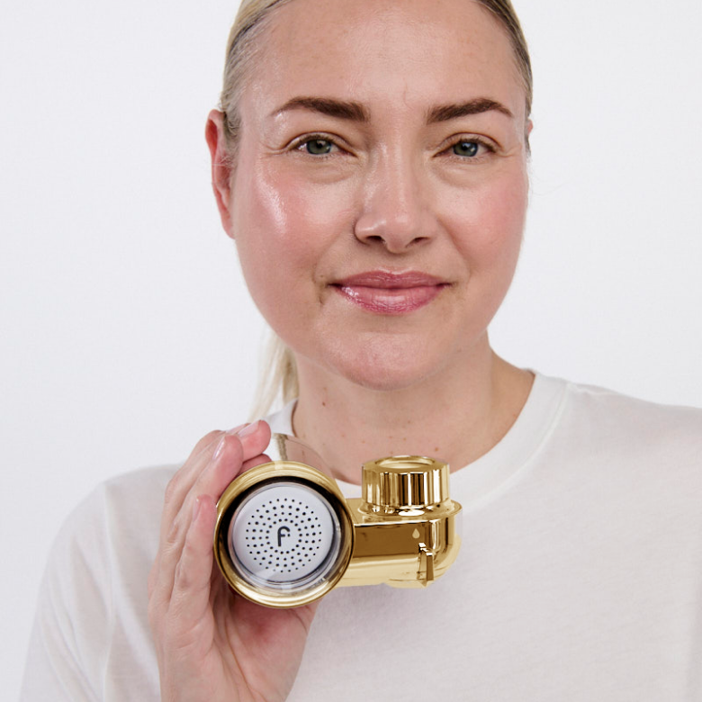 Person holding a gold shower filter against a white background.