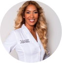 Person in a white coat smiling against a plain background.