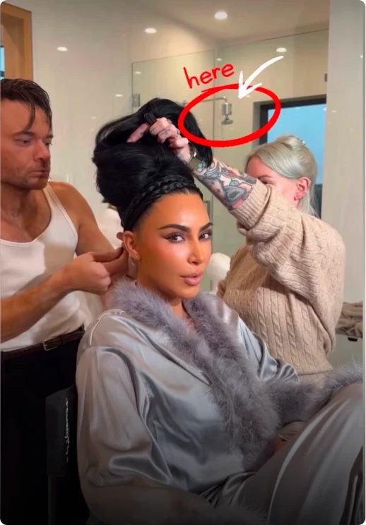 Kim Kardashian in a grey feathered robe gets her hair styled by two people.
