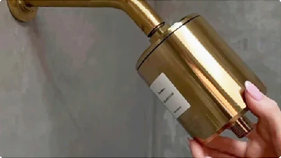 A close-up of a person's hand installing a gold-colored shower filter onto a shower arm.