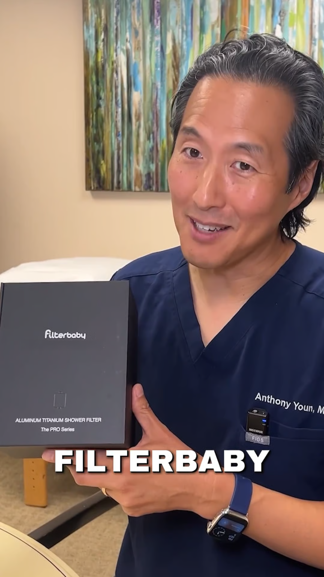 A man in blue scrubs holds a black box for a Filterbaby shower filter.