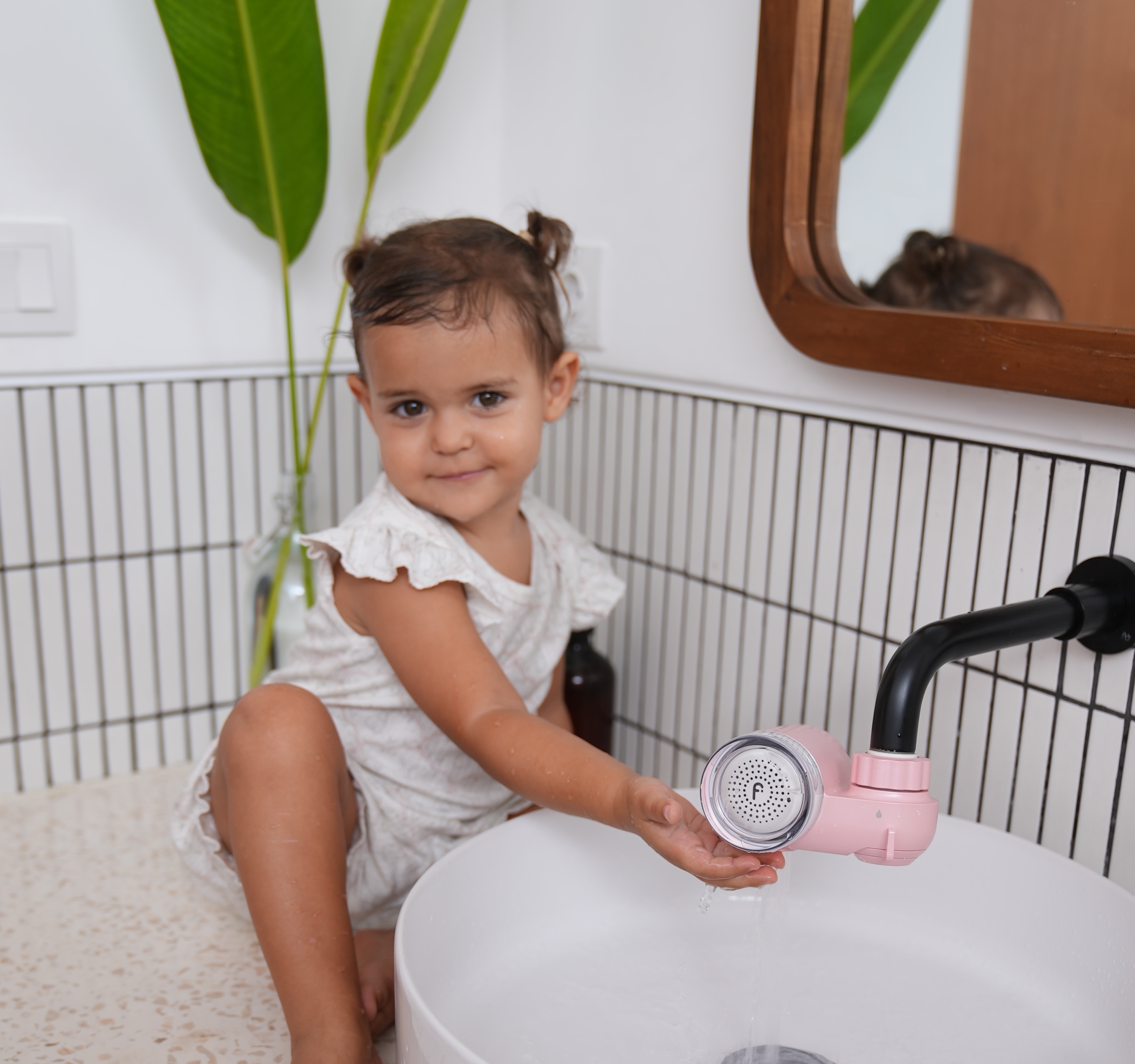 Child sitting on a bathroom counter, playing with water from a faucet.