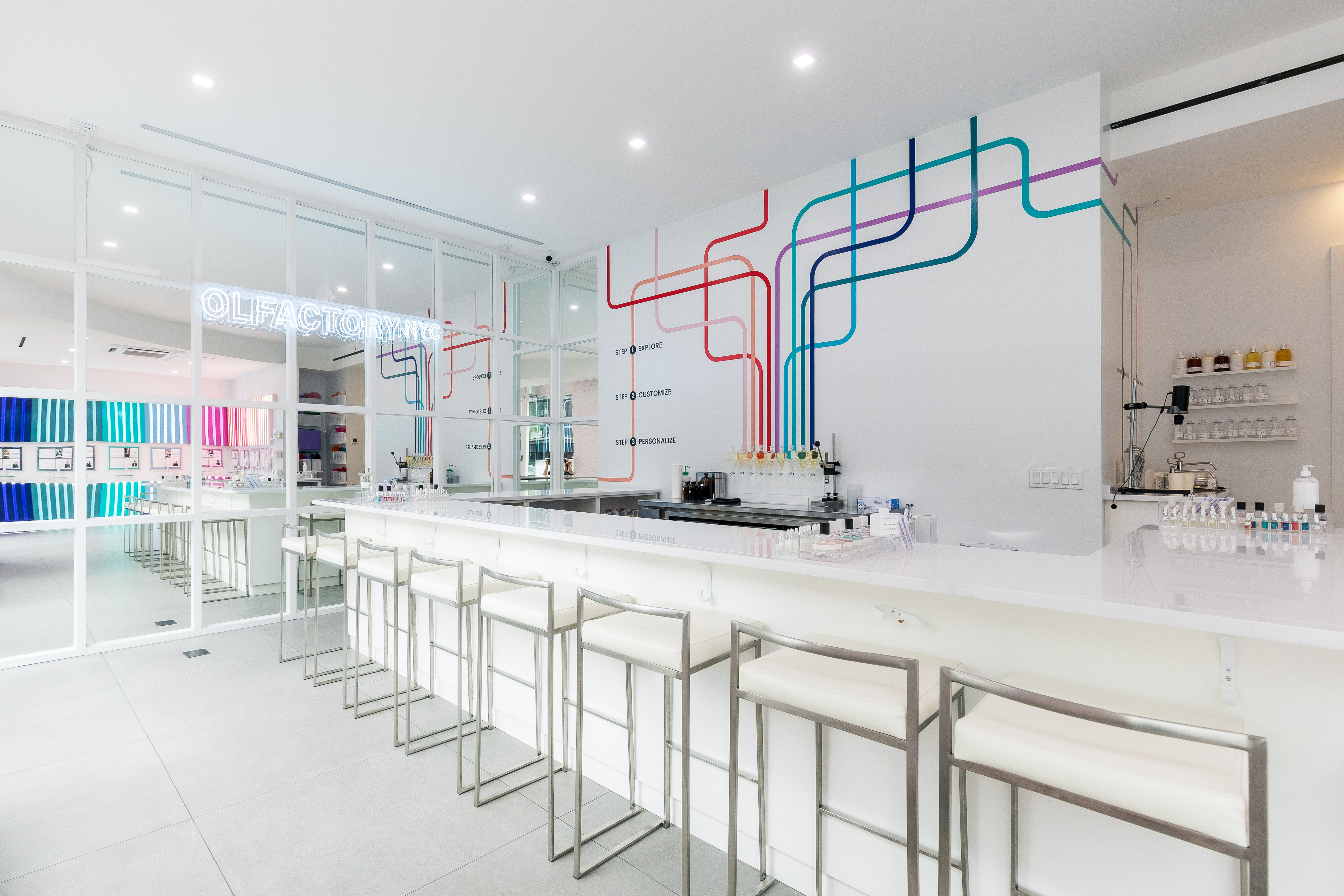 Modern perfume bar with colorful wall design and white seating.