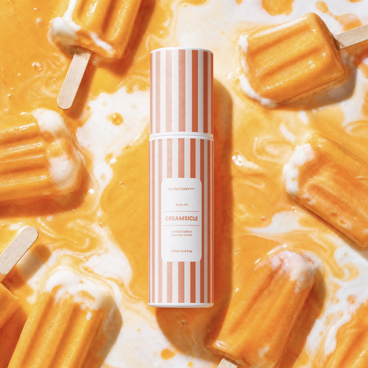 A striped bottle of Creamsicle body oil surrounded by melting orange and cream popsicles.