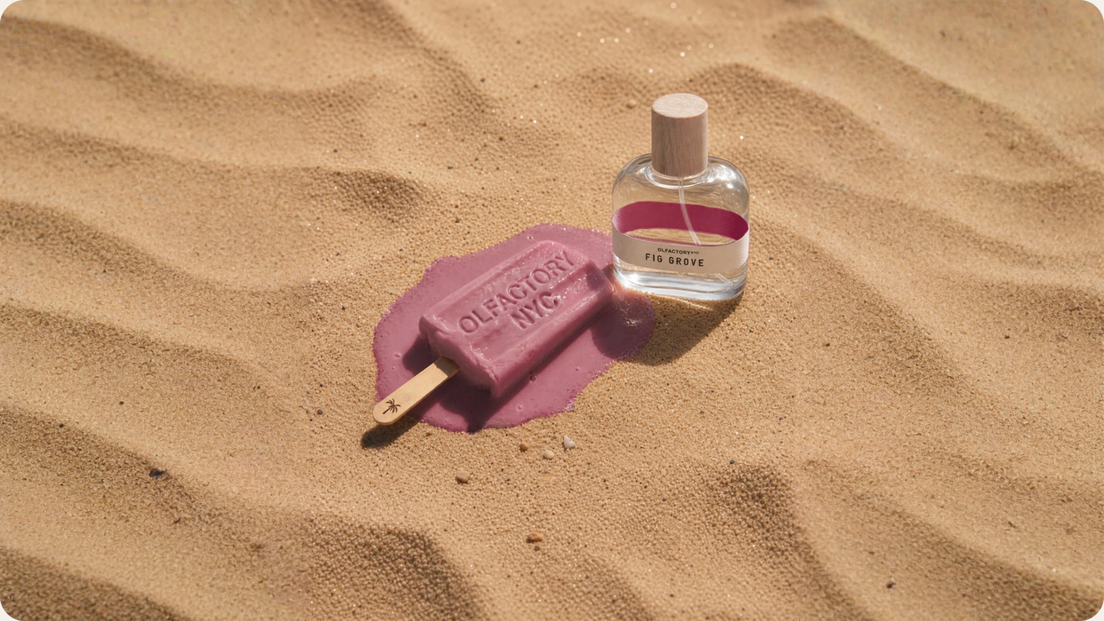 A bottle of perfume and a melting purple popsicle with the words Olfactory NYC sit on sand.