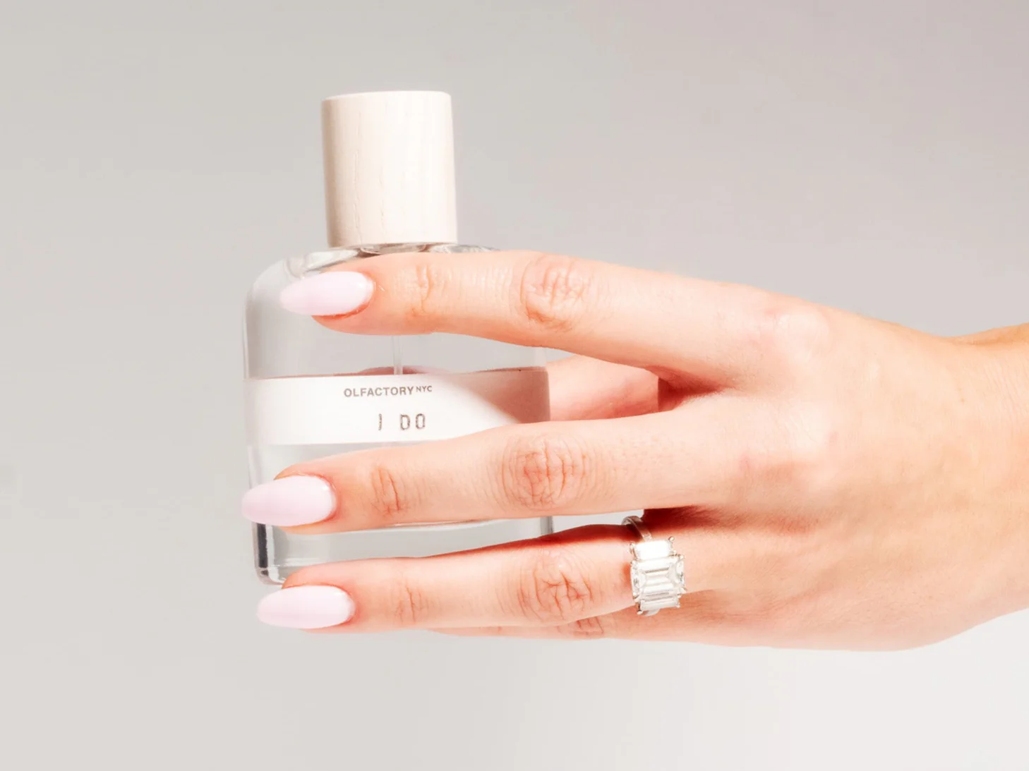 Hand with pink nails holding a perfume bottle labeled 'I DO.'