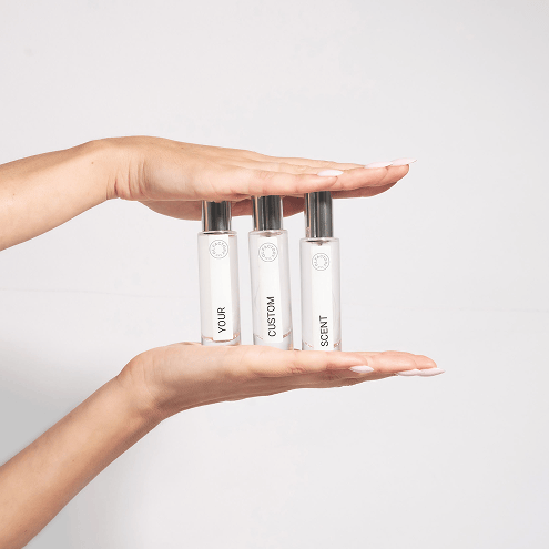 Hands holding three small white bottles labeled 'Your Custom Scent'.