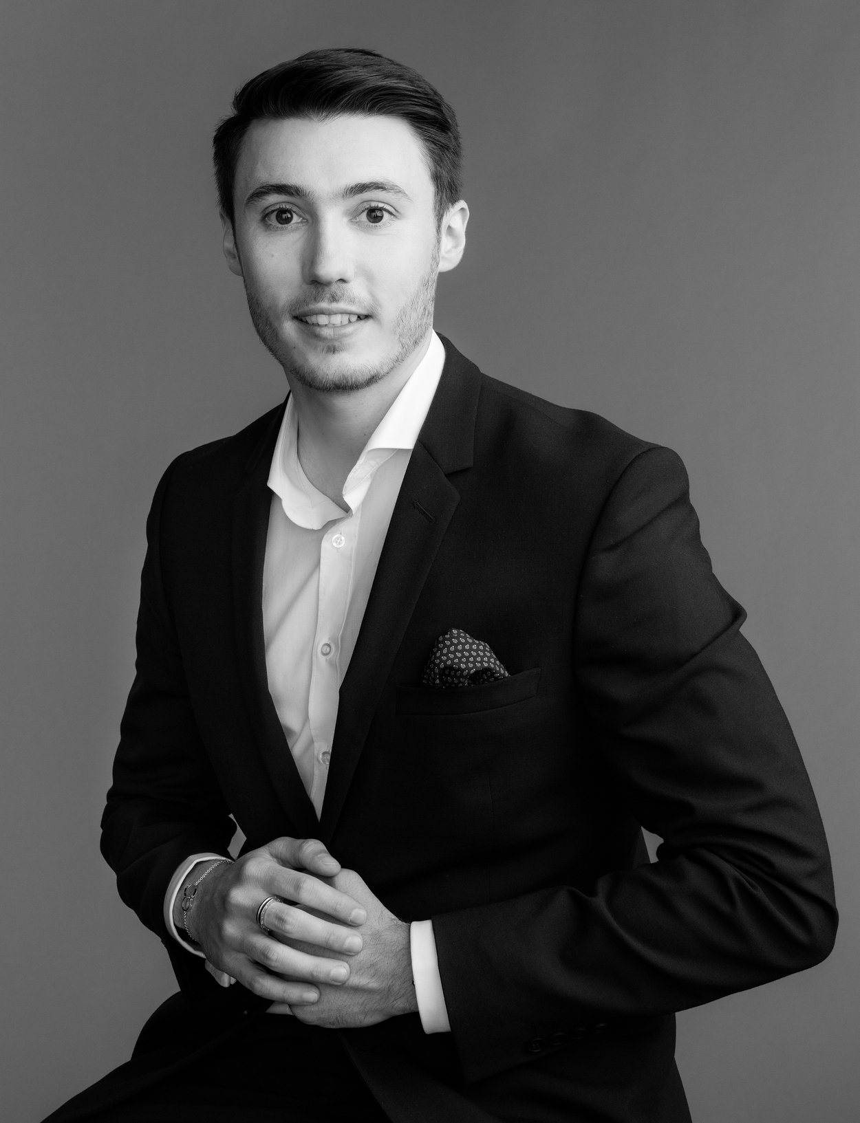 Black and white portrait of a man in a suit, seated and smiling.