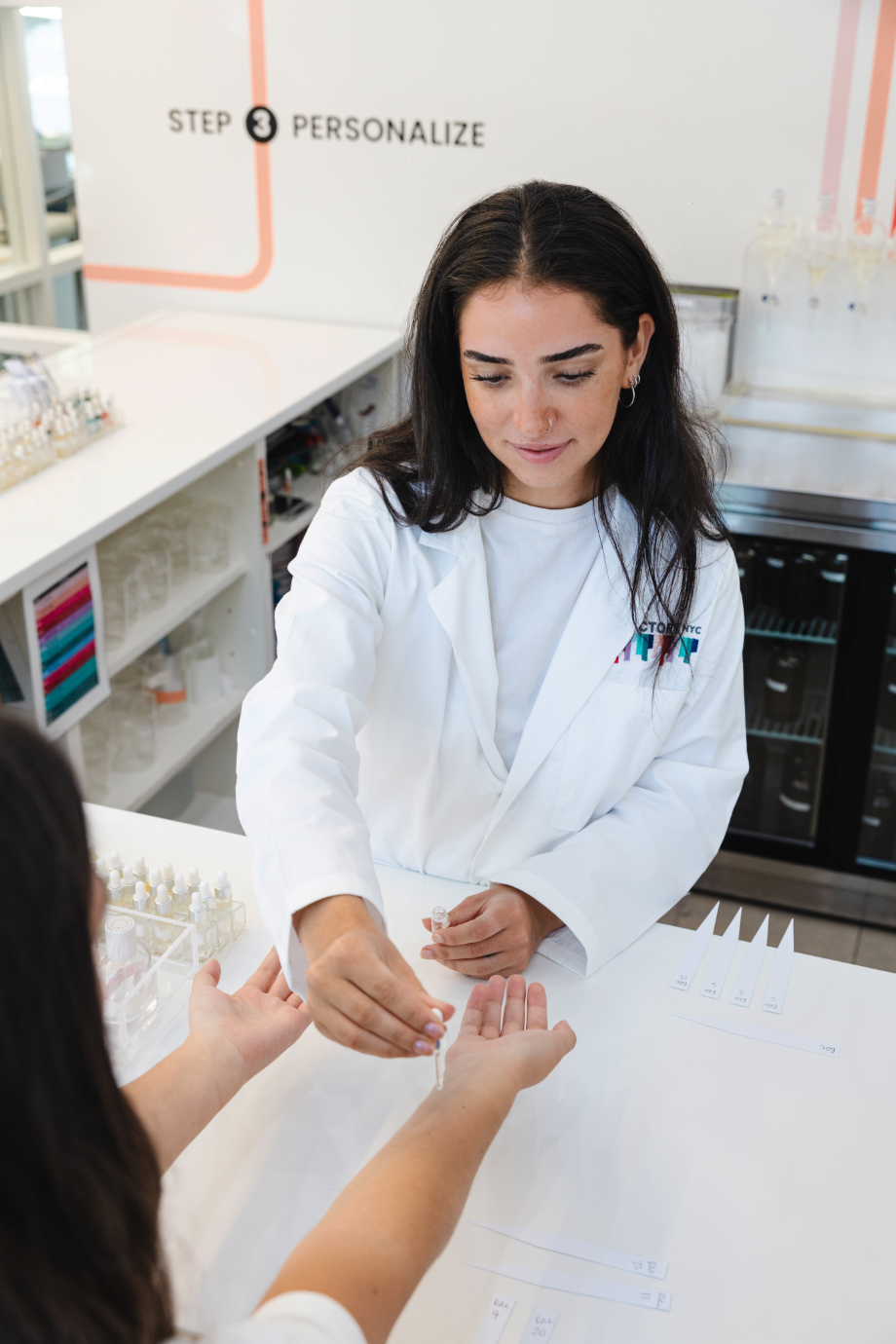 Woman in lab coat applying liquid to another person's wrist.