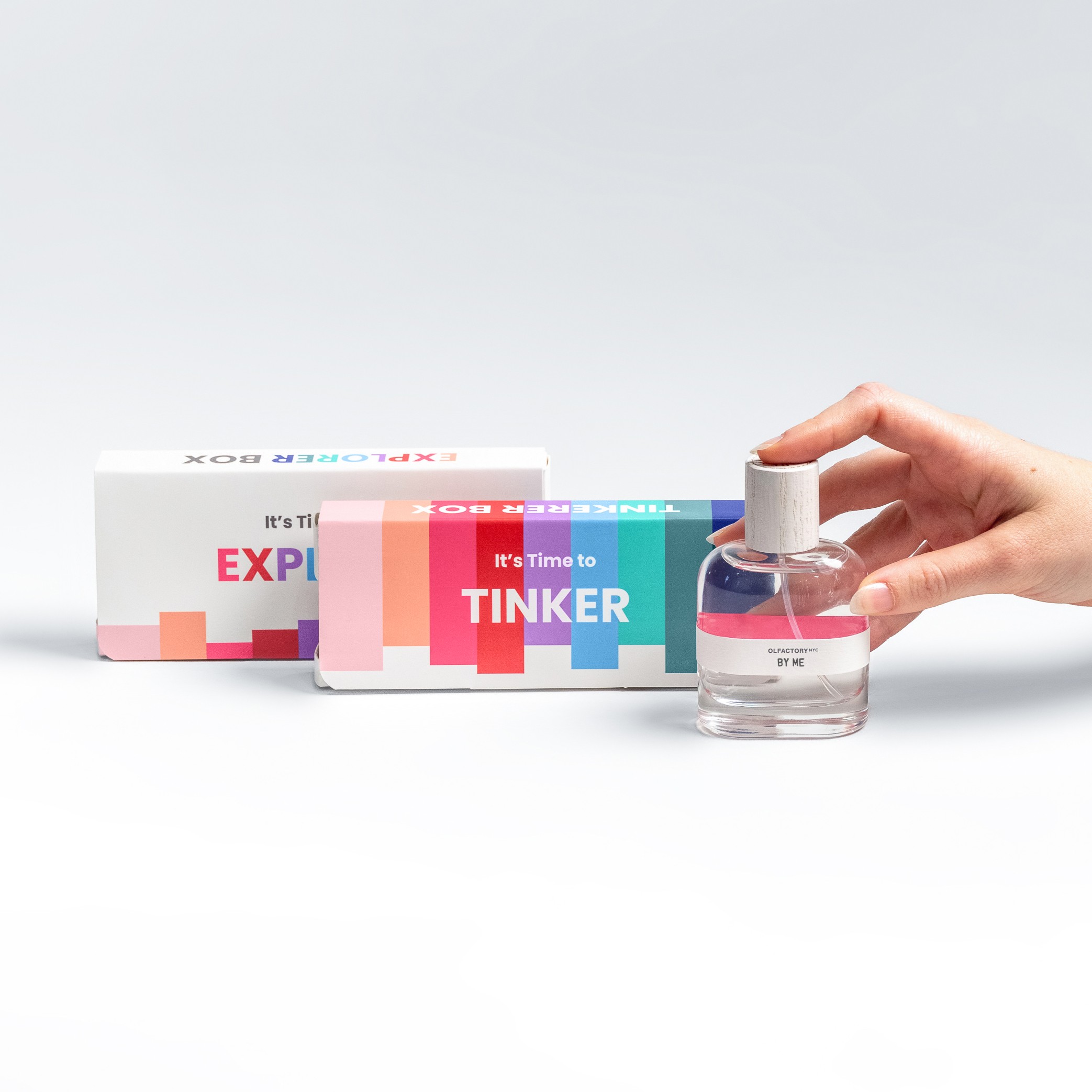 Hand holding a small, clear bottle in front of colorful boxes labeled 'Explore' and 'Tinker'.