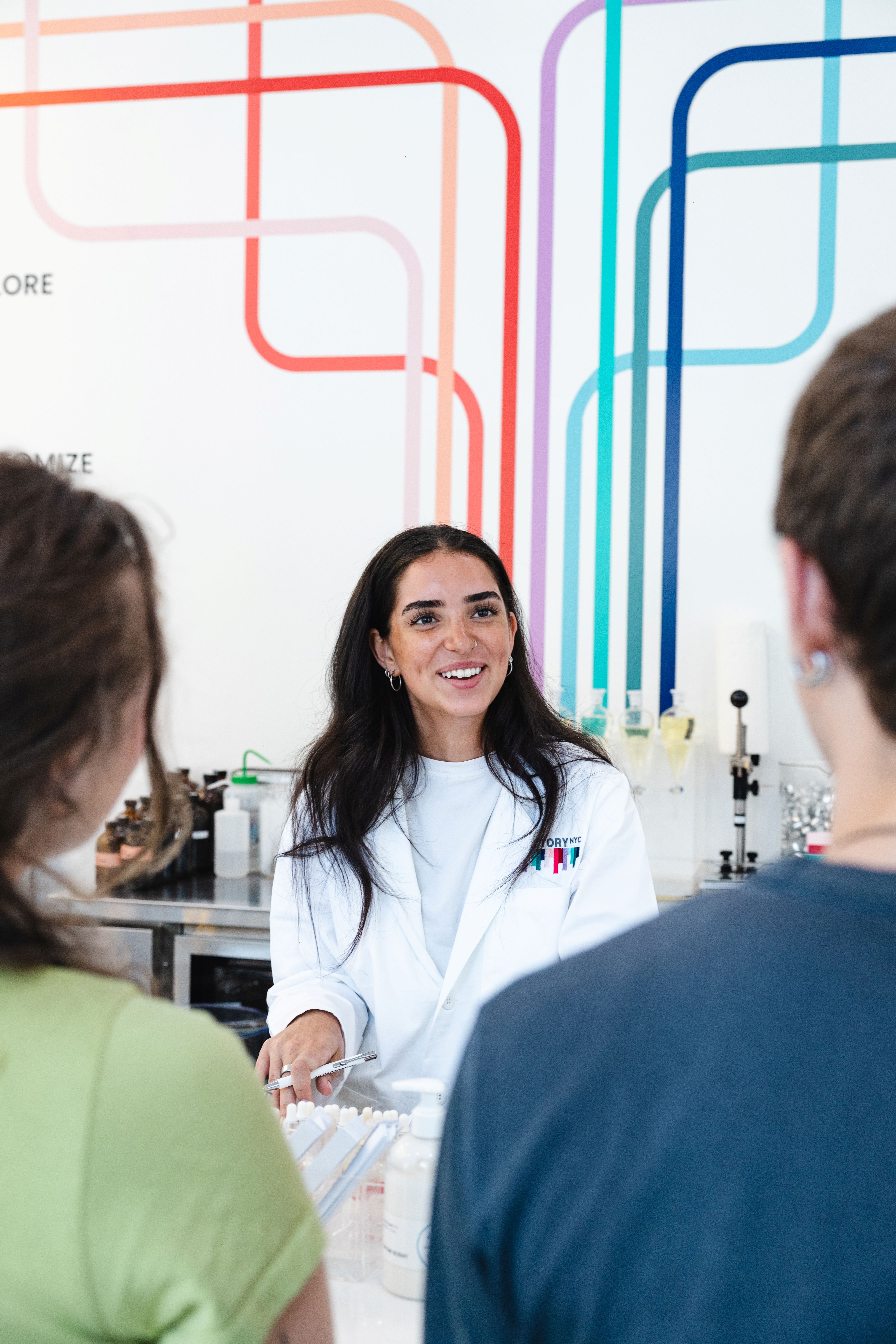 Woman in a lab coat smiling and talking to two people.