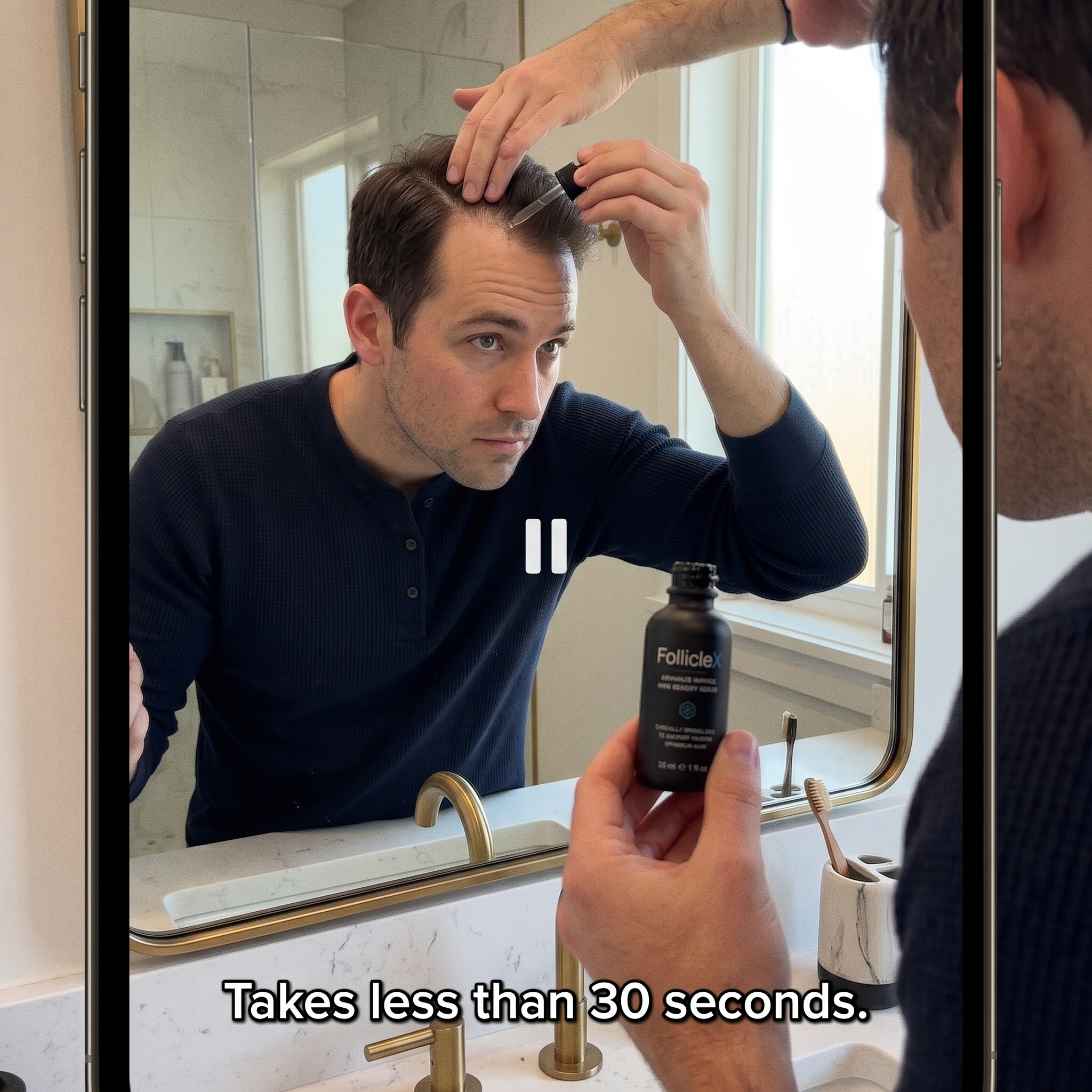 A man looks in a bathroom mirror while applying a hair serum to his scalp with a dropper.