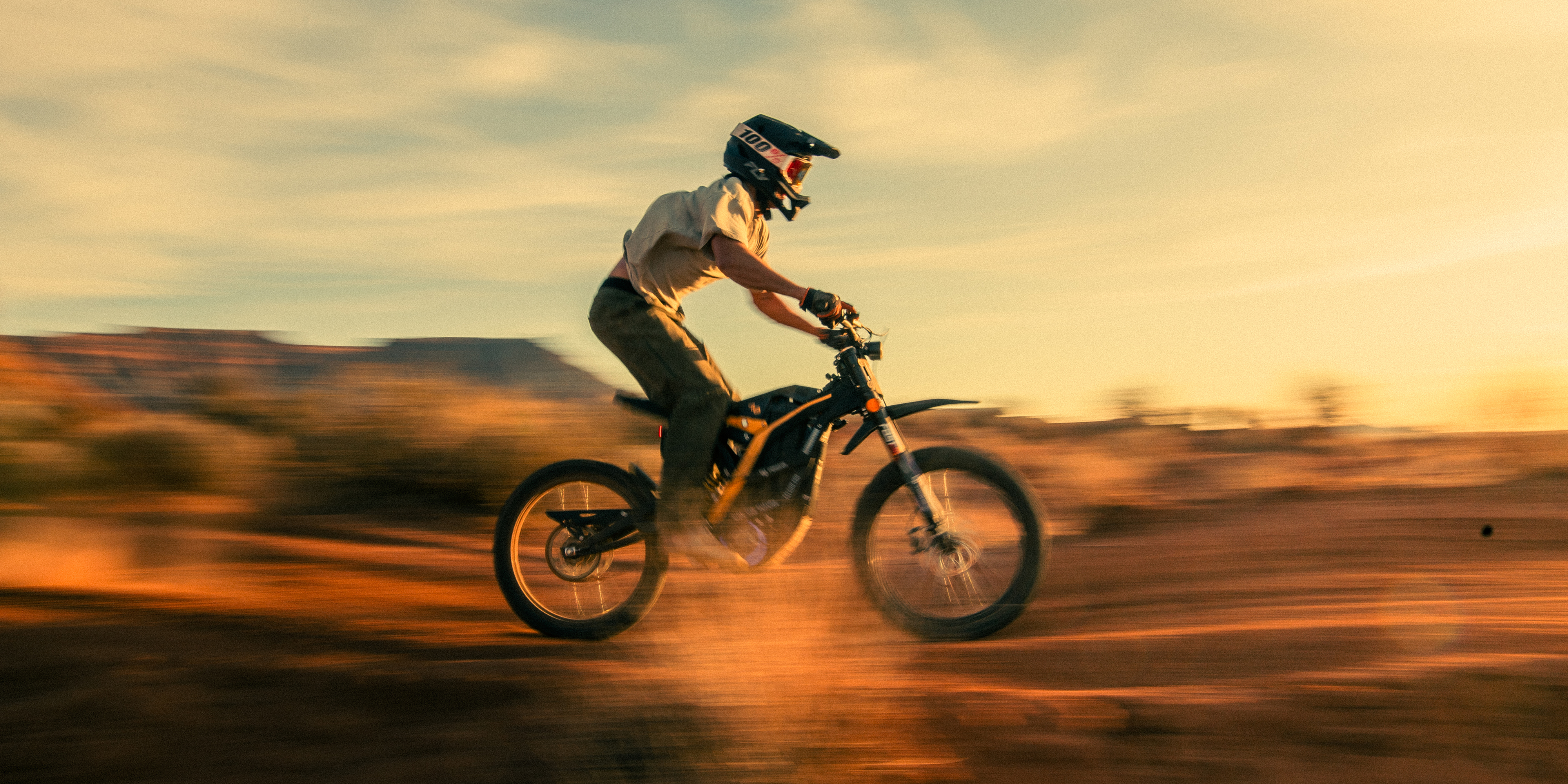 Person riding a dirt bike in a desert landscape at sunset.