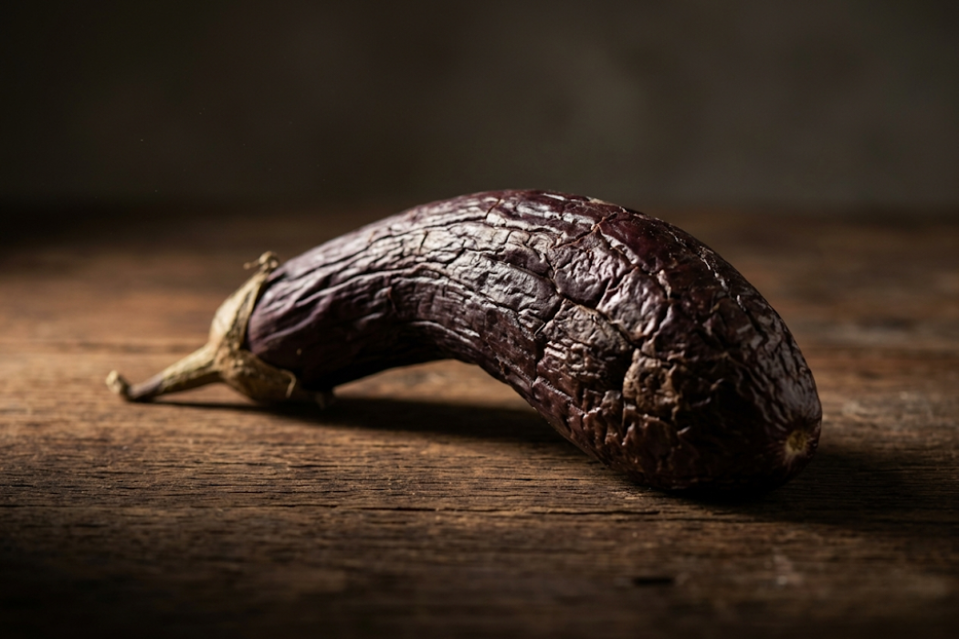 A close-up shot of a shriveled, rotting eggplant with wrinkled skin, resting on a rustic wooden surface.