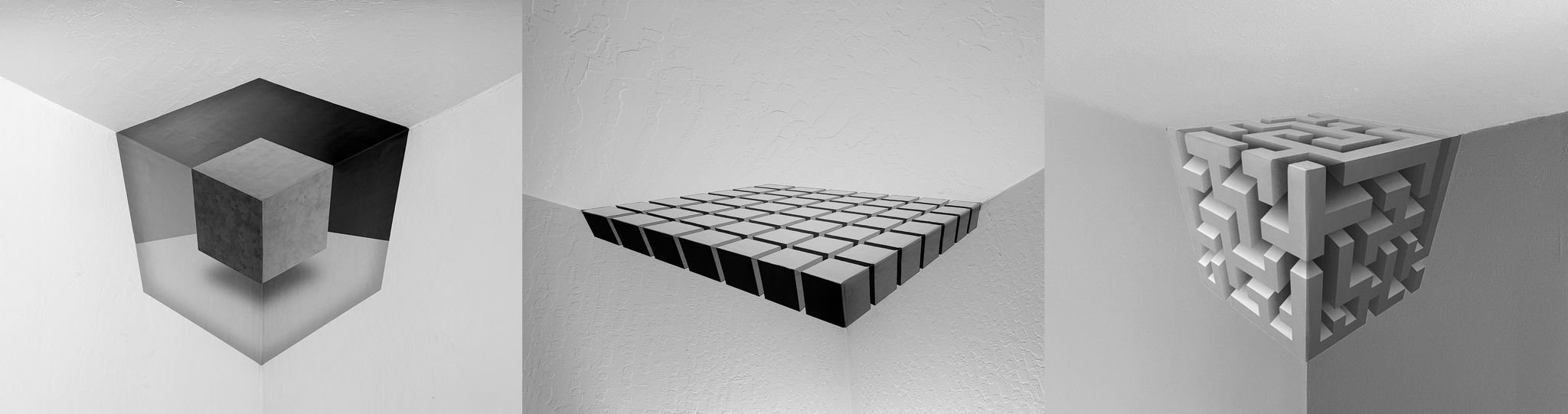 Three black and white geometric wall sculptures in a corner, featuring cubes and maze-like patterns.