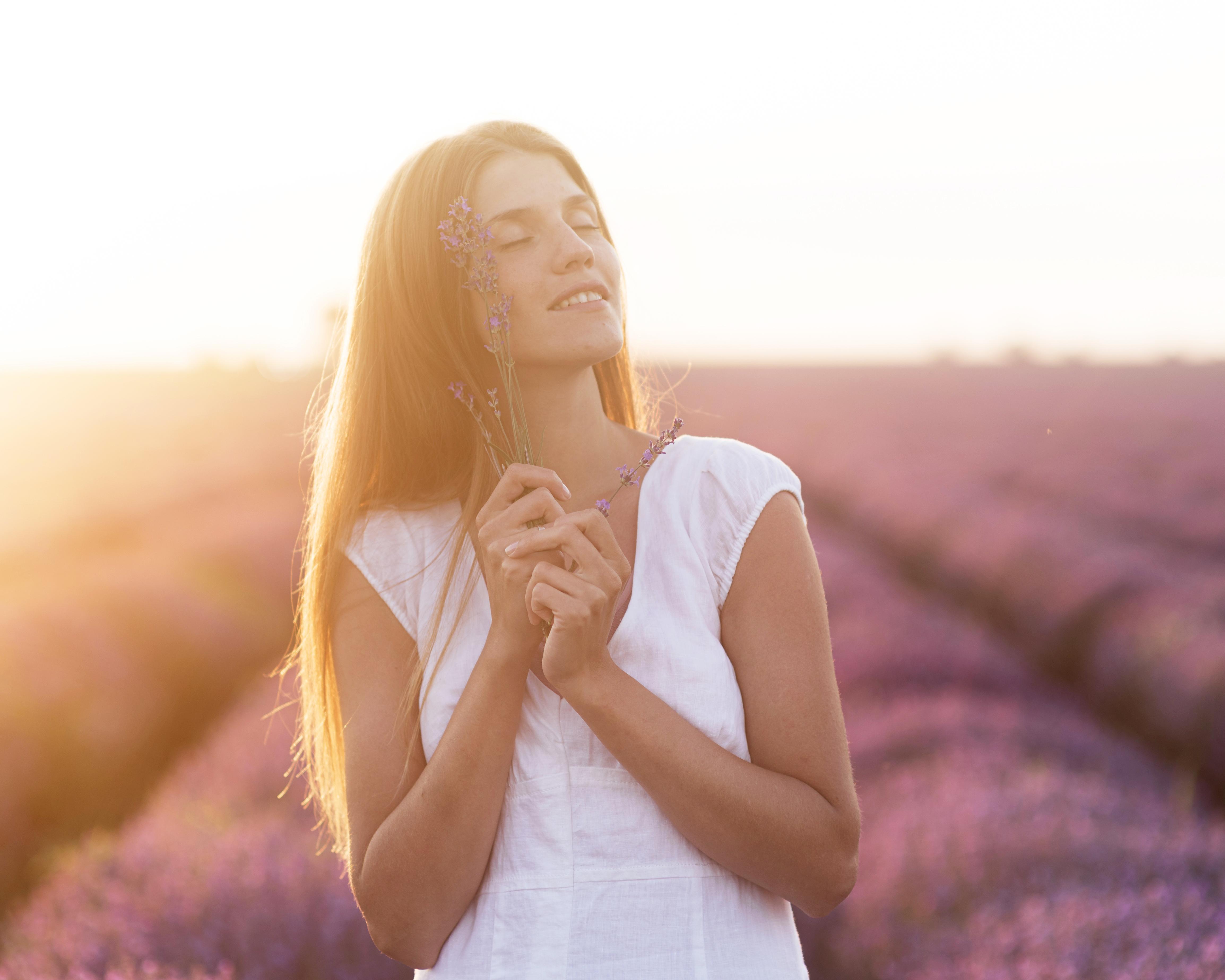Woman in white dress holding lavender in a sunlit field.