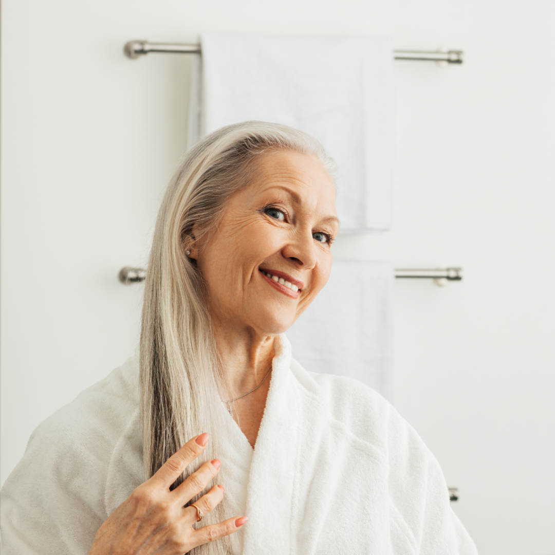 Smiling person in a white bathrobe near a towel rack.