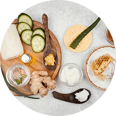 An overhead view of natural skincare ingredients like cucumber, ginger, aloe, and honeycomb on a light surface.