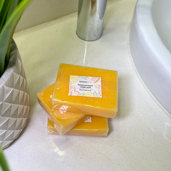 Three yellow soap bars stacked on a bathroom counter near a plant and sink.