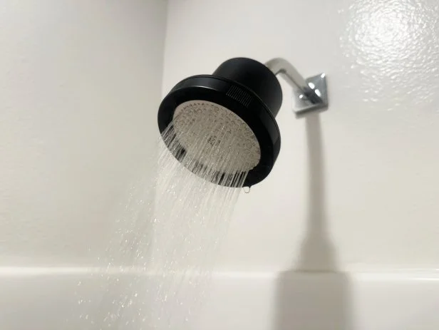 Black showerhead spraying water in a white-tiled bathroom.