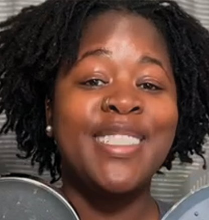 Person smiling, holding two round objects, with a striped background.