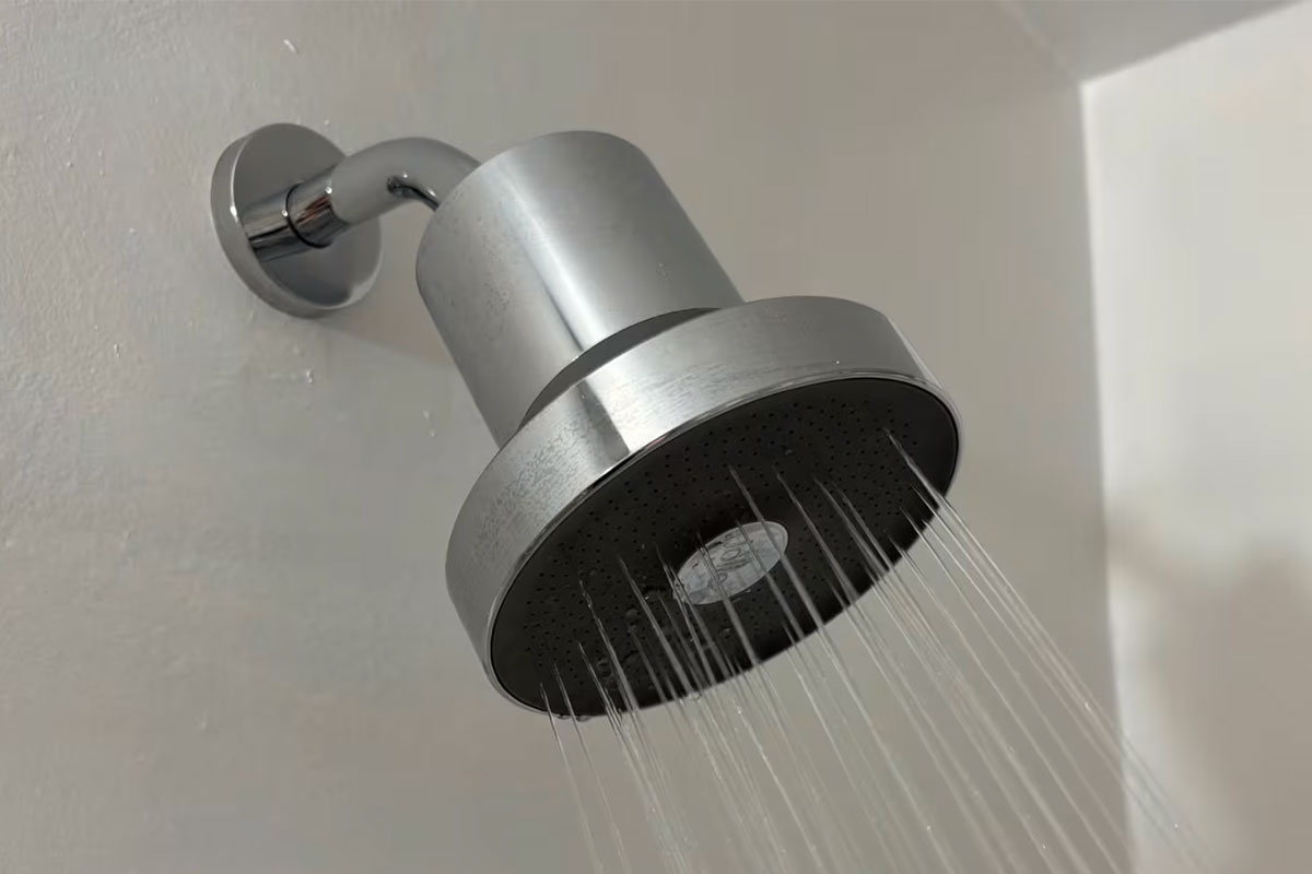 A metal showerhead with water spraying in a bathroom.