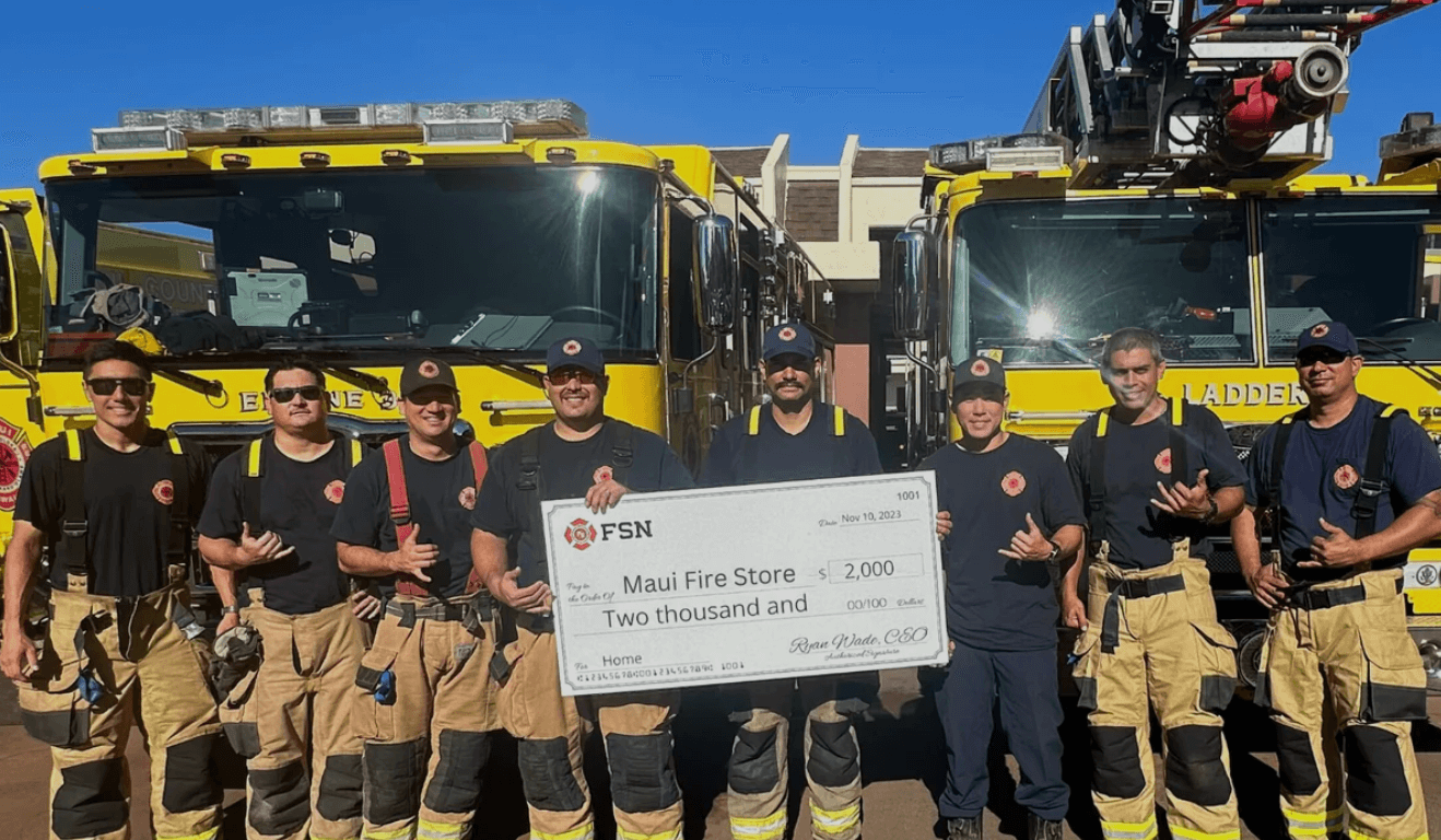 Firefighters holding a large check in front of yellow fire trucks.