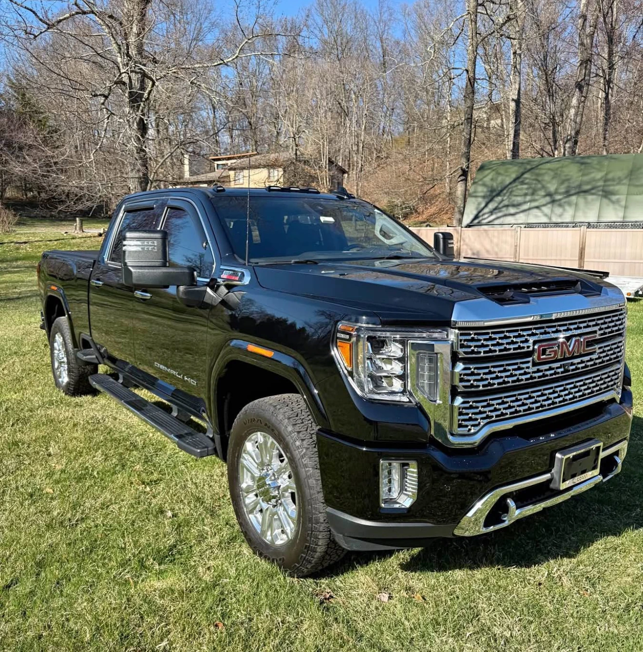 Black GMC truck parked on grass with trees and a building in the background.
