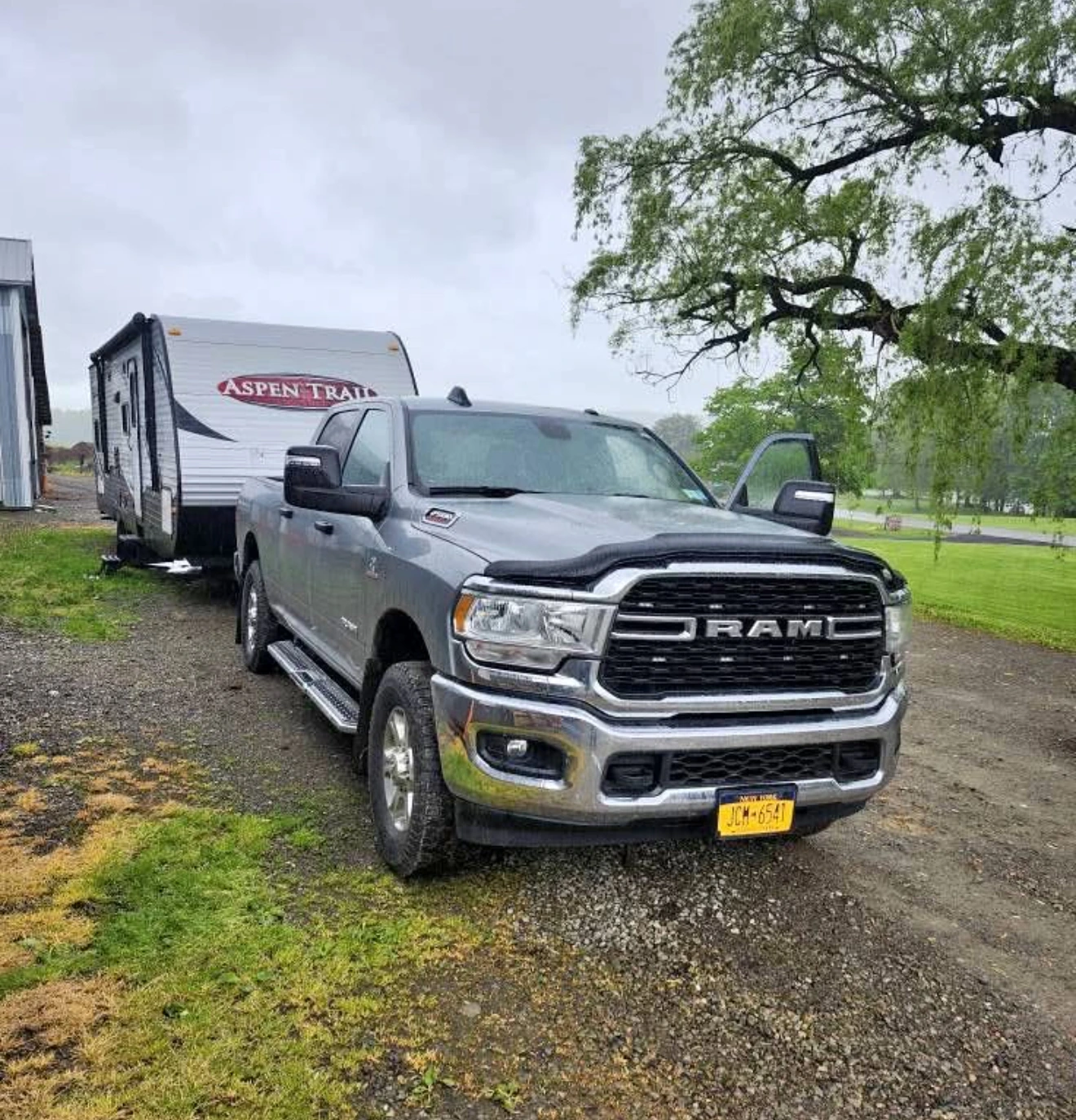 A gray RAM truck towing an Aspen Trail trailer on a gravel path.
