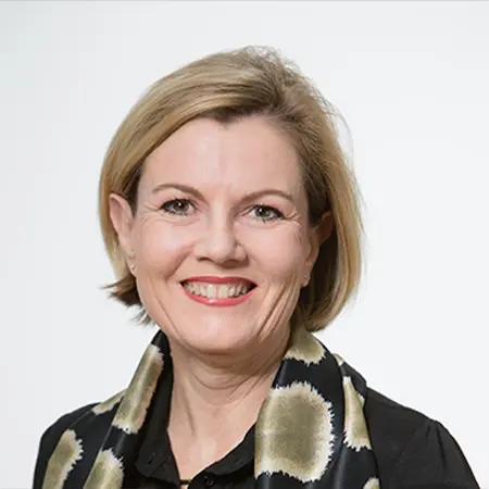 Smiling person with short blonde hair and patterned scarf on white background.