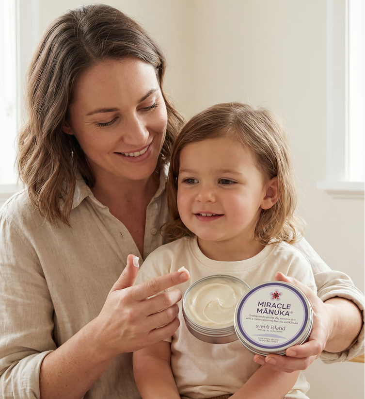 A woman holding a young child prepares to apply a dab of cream from an open tin.