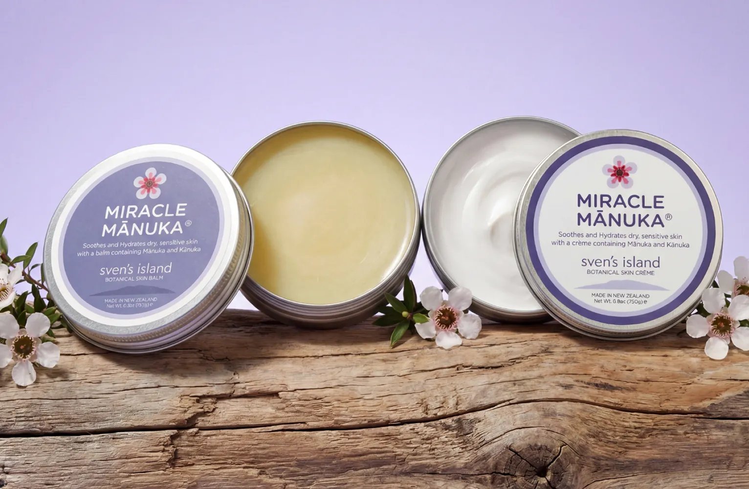 Two open tins of Miracle Mānuka skin balm and cream on a log with small white flowers.