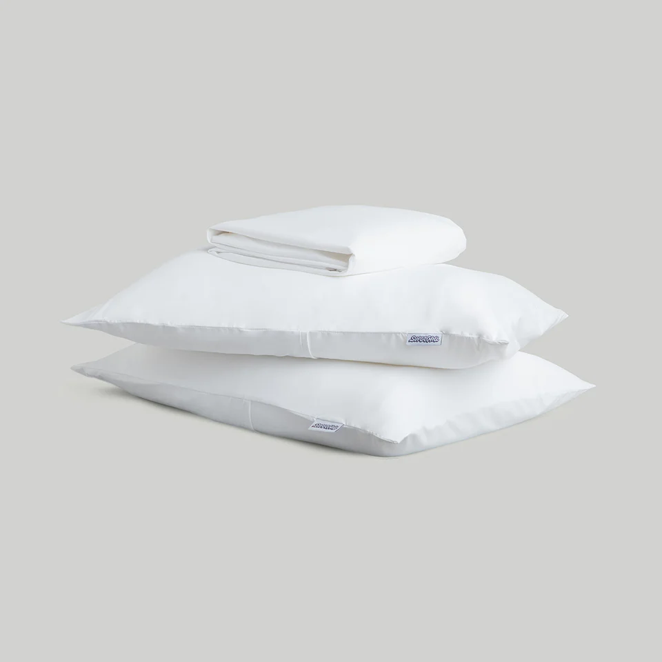 A stack of two white pillows with a folded white sheet on top against a gray background.