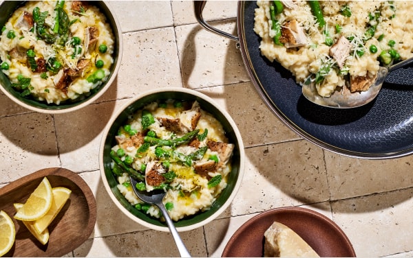 Bowls of risotto with chicken, peas, and asparagus on a tiled surface.