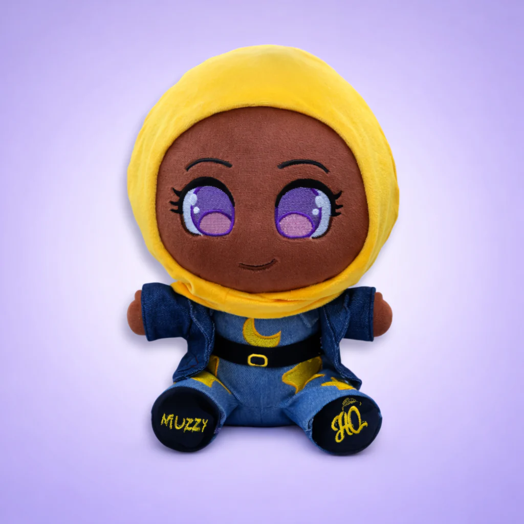 A plush doll with brown skin, large purple eyes, and a yellow headscarf, wearing a denim outfit.