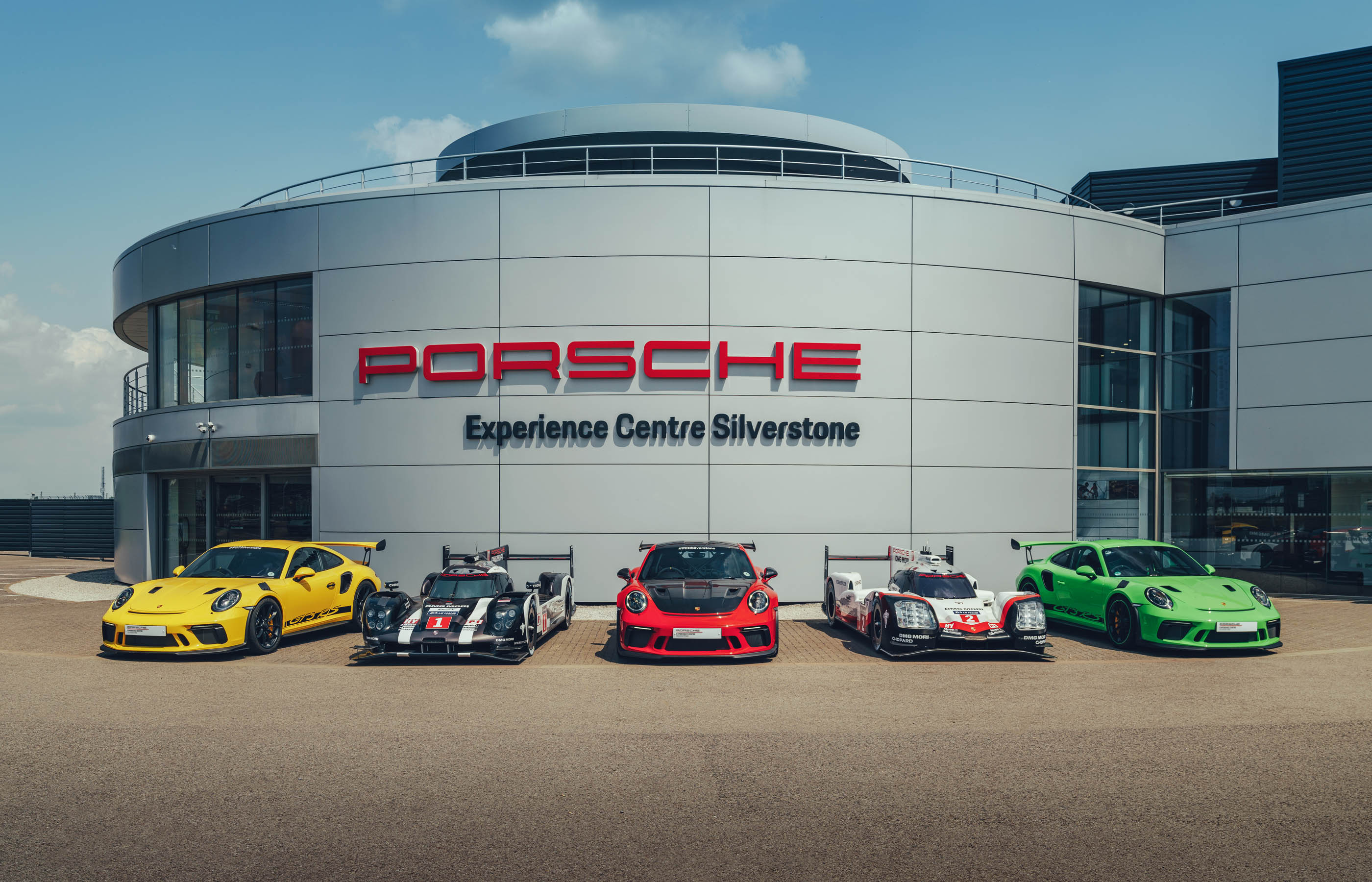 Five Porsche cars parked in front of Porsche Experience Centre Silverstone.