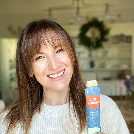 Person smiling and holding a product tube in a well-lit room.